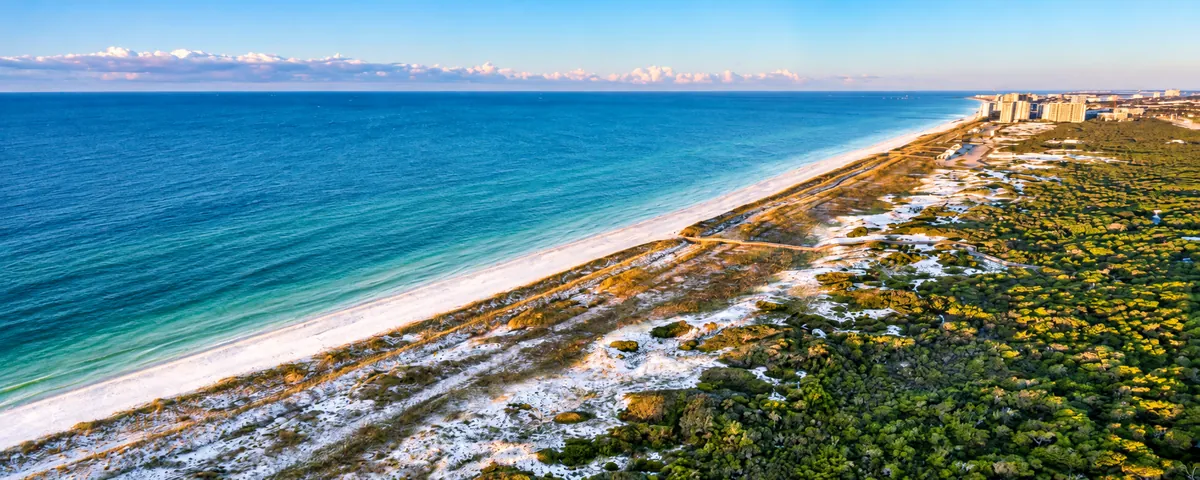 Aerial view of white sand dunes and coastal scrub along a turquoise Gulf shoreline